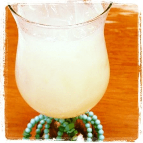 A refreshing drink in a tall glass filled with ice, sitting on a wooden table, adorned with colorful beads.