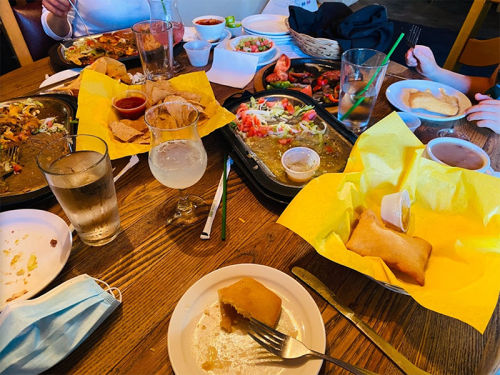 A table filled with various dishes, drinks, and utensils, featuring colorful plates of food and a mask nearby.