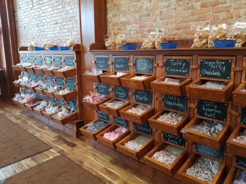 A candy shop display with wooden bins filled with various taffy and sweets, labeled with chalkboard signs.