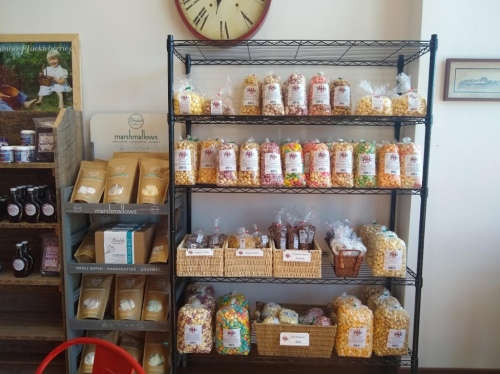 A display shelf filled with various jars and bags of colorful candies, popcorn, and marshmallows in a shop.