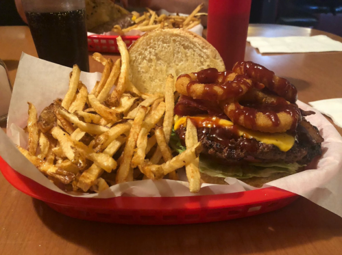 A juicy burger topped with onion rings and cheese, served with a side of crispy fries in a red basket.