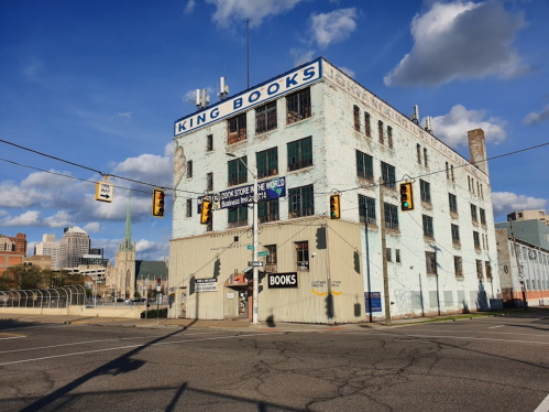 A large, weathered building with "King Books" signage, set against a blue sky with clouds and city skyline in the background.