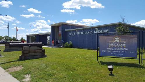 Exterior of the Dossin Great Lakes Museum with a sign for free admission and a cannon in the foreground.