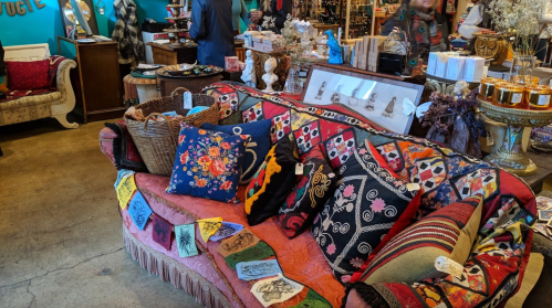 A colorful, patterned couch adorned with decorative pillows, surrounded by eclectic decor in a vibrant shop.