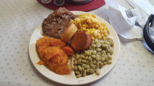 A plate of food featuring macaroni and cheese, cornbread, sweet potatoes, lima beans, and a serving of beans.