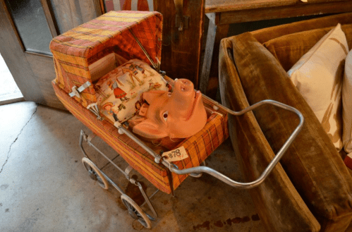A vintage stroller with a pig-shaped head and colorful fabric, placed next to a green couch in a cozy setting.