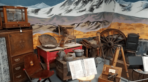 A collection of vintage items, including furniture and tools, set against a mural of mountains.