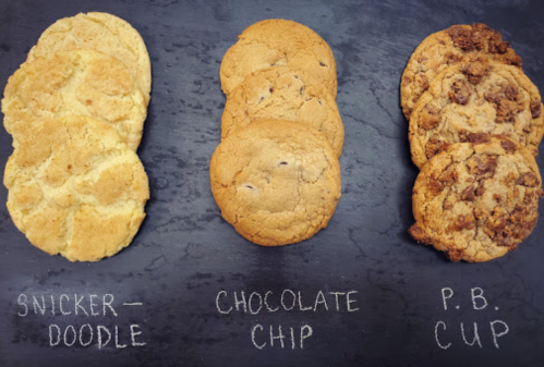 Three types of cookies on a slate: Snickerdoodle, Chocolate Chip, and P.B. Cup, labeled with chalk.