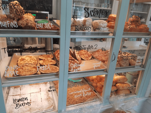 Display case filled with various baked goods, including muffins, scones, and loaf cakes, with handwritten labels.