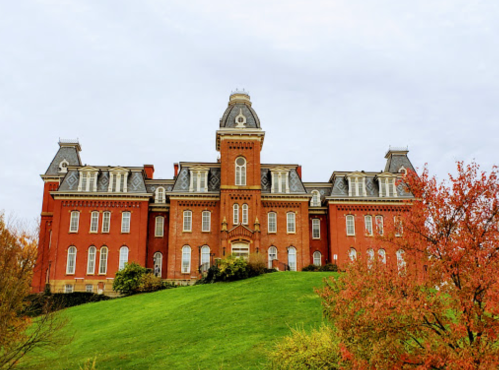 Historic red brick building with ornate architecture, set on a green hill with autumn foliage in the foreground.