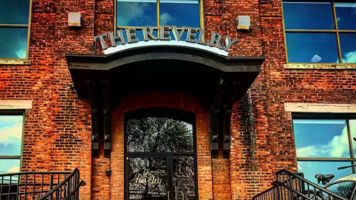 Entrance of The Revelry, a brick building with large windows and a sign above the door.