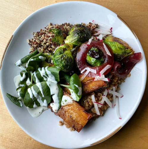 A plate of quinoa, roasted Brussels sprouts, spinach, pickled onions, and sweet potato drizzled with a creamy dressing.