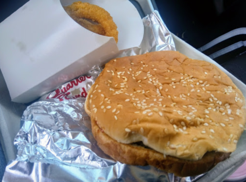 A sesame seed bun sandwich next to a box of onion rings, all placed on a tray.