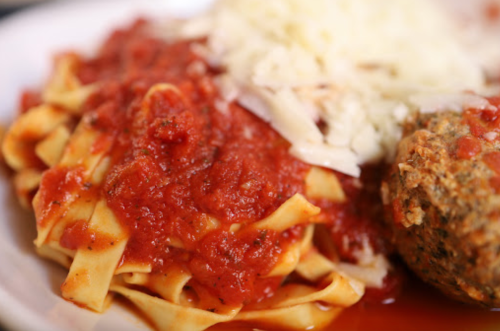 A plate of fettuccine pasta topped with marinara sauce, grated cheese, and a meatball on the side.