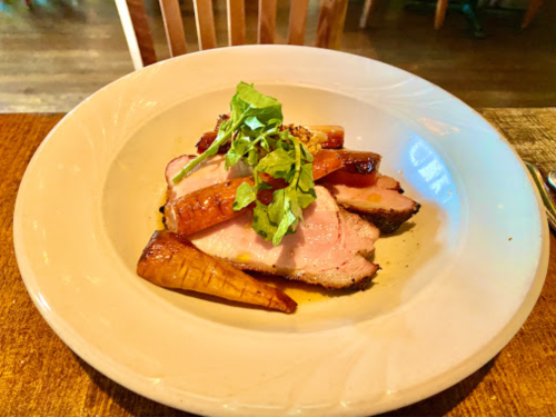 A plate of sliced roasted meat garnished with arugula and accompanied by roasted carrots.