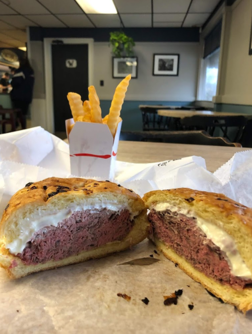 A sliced sandwich with pink meat and creamy filling, alongside a small container of crispy French fries.