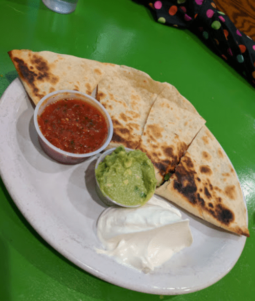 A plate with quesadillas, salsa, guacamole, and sour cream on a bright green table.