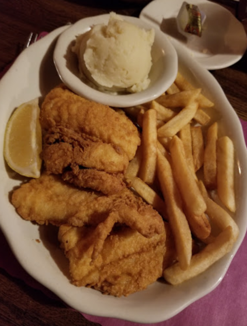 A plate of fried fish fillets, French fries, and a serving of mashed potatoes with a lemon wedge on the side.