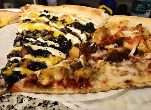 A slice of pizza divided into two halves: one topped with meat and drizzled sauce, the other with chicken and cheese.