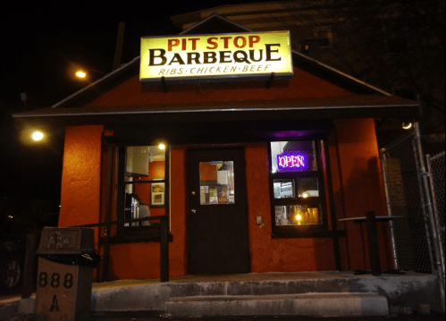 A brightly lit barbecue restaurant at night, featuring a sign that reads "Pit Stop Barbeque" and an "Open" neon sign.