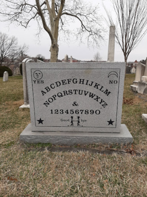 A gravestone featuring the alphabet, numbers, and symbols, with "YES" and "NO" at the top, set in a cemetery.