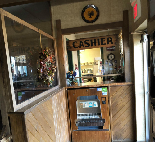 A rustic cashier area with a wooden sign, vintage decor, and a vending machine in a cozy setting.