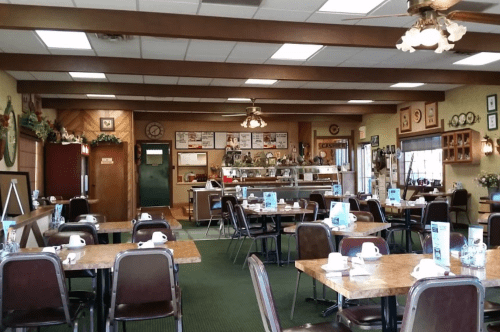 A cozy diner interior with wooden beams, tables set for dining, and a counter displaying menu items.