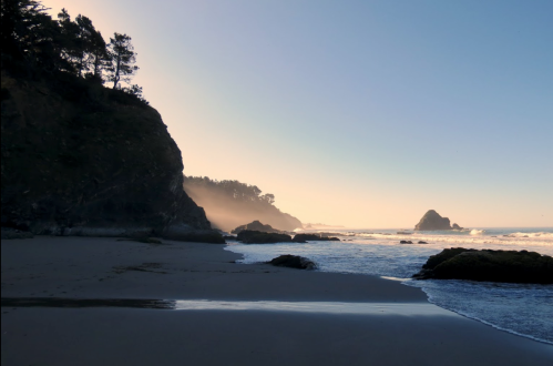 A serene beach scene at dusk, featuring rocky cliffs, gentle waves, and a misty horizon.