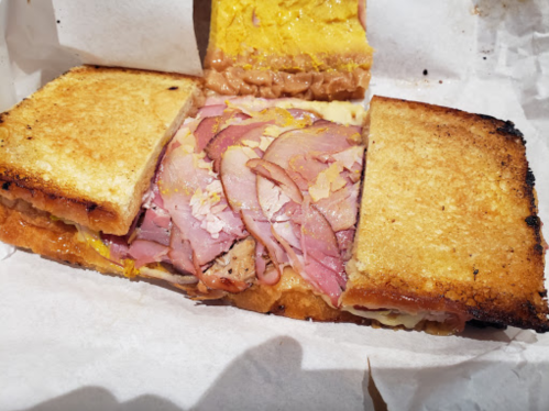 A toasted sandwich filled with layers of ham, cheese, and mustard, cut in half and served on white paper.