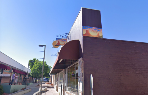 A corner building with a sign for a café, featuring a brown awning and clear blue sky above.