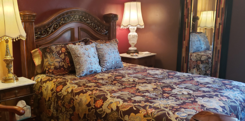 A cozy bedroom featuring a floral-patterned bedspread, decorative pillows, and elegant lamps beside a mirrored wardrobe.