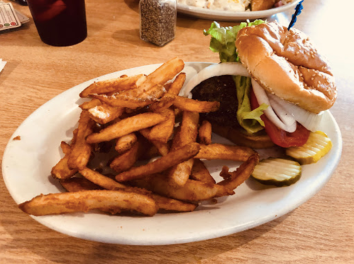 A plate with a hamburger topped with lettuce, tomato, and onion, served with a side of crispy French fries and pickles.