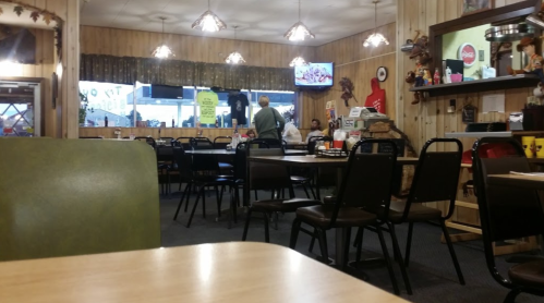 A cozy diner interior with empty tables, a TV on the wall, and a few customers in the background.