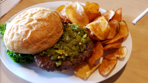 A plate with a burger topped with green peppers, lettuce, and a side of crispy potato chips.
