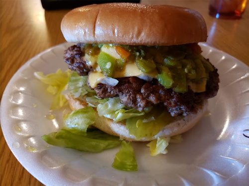 A juicy burger with melted cheese, green peppers, and lettuce on a bun, served on a paper plate.