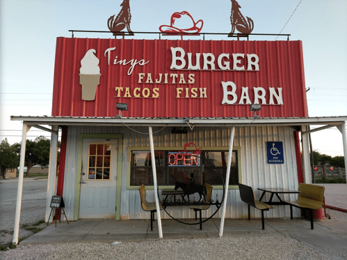 A colorful diner named "Tiny's Burger Barn" featuring signs for burgers, fajitas, tacos, and fish, with an open sign.