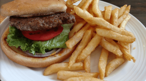 A plate featuring a hamburger with lettuce, tomato, and onion, alongside a serving of golden French fries.