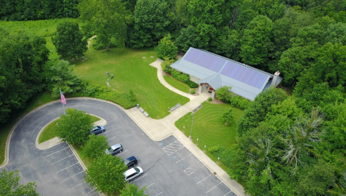 Aerial view of a building surrounded by trees, with a parking lot and an American flag nearby.