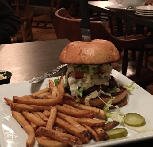A juicy burger topped with lettuce and tomato, served with crispy fries and pickles on a wooden table.