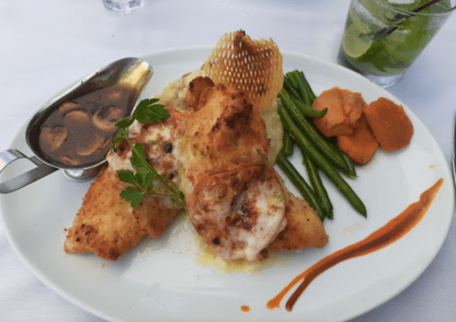 A plate of fried fish with shrimp, mashed potatoes, green beans, and a side of sauce, garnished with parsley.