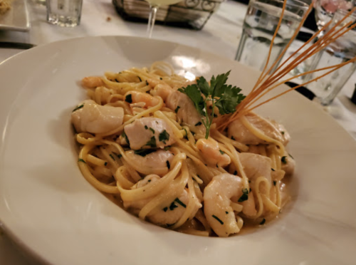 A plate of linguine pasta with shrimp, garnished with herbs and decorative pasta strands, served in a restaurant setting.