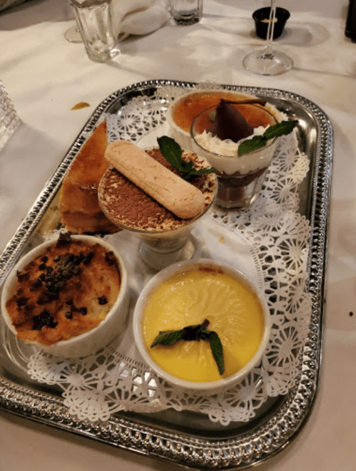 A silver tray with four dessert dishes: crème brûlée, tiramisu, lemon custard, and a chocolate mousse, garnished with mint.