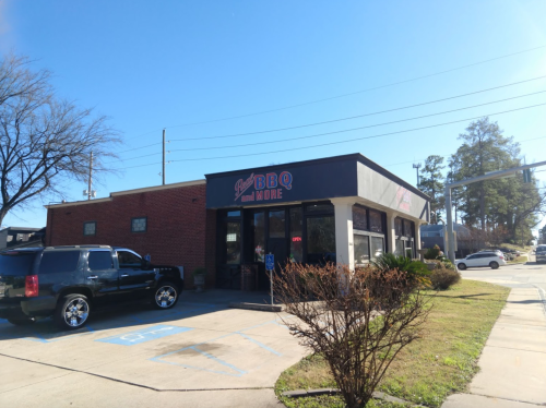 A BBQ restaurant with a sign reading "Just BBQ and More," featuring a black SUV parked outside on a sunny day.