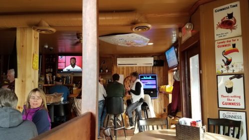 A cozy bar interior with patrons at the counter, TVs showing sports, and Guinness advertisements on the walls.