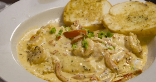 A creamy shrimp dish with vegetables, served with two slices of toasted garlic bread on the side.