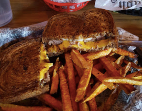 A grilled cheese sandwich with melted cheese, served with a side of crispy sweet potato fries in a basket.