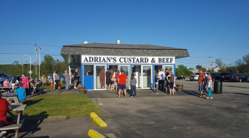 A busy outdoor scene at Adrian's Custard & Beer, with a crowd gathered outside on a sunny day.