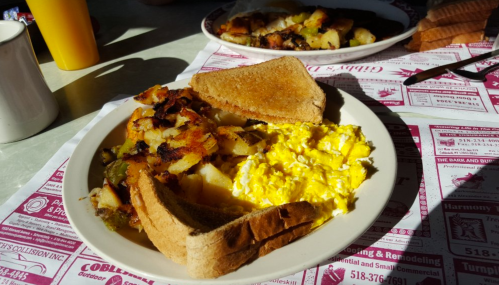 A plate of scrambled eggs, crispy potatoes, and two slices of toast on a table with menus underneath.