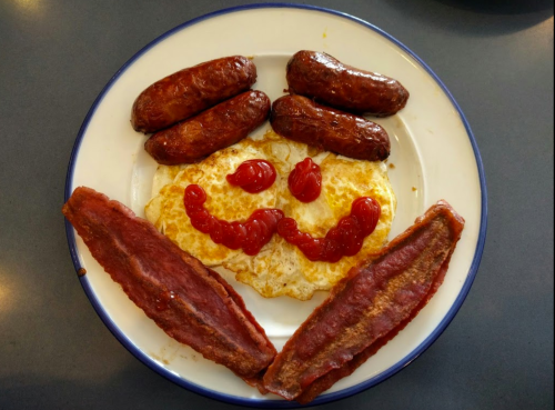 A plate with a smiley face made of an egg, ketchup, sausages, and bacon.