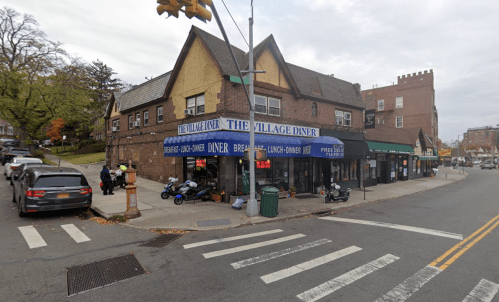 A corner diner with a blue awning, surrounded by trees and parked cars on a busy street.